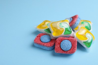 Photo of Many dishwasher detergent tablets and pods on light blue background, space for text