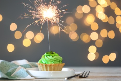 Cupcake with burning sparkler on table against blurred festive lights. Space for text