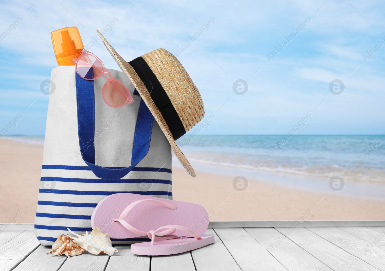 Image of Stylish bag with beach accessories on wooden surface near seashore. Space for text