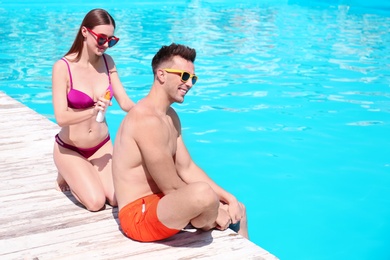 Young woman applying sun protection cream onto boyfriend at swimming pool
