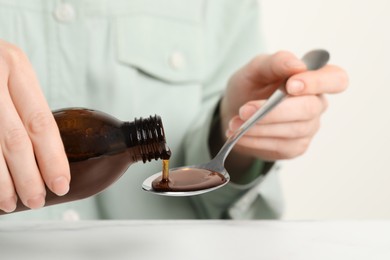 Woman pouring syrup from bottle into spoon at table, closeup. Cold medicine