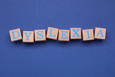 Photo of Wooden cubes with word Dyslexia on blue background, flat lay