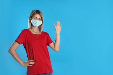 Photo of Woman in protective mask showing hello gesture on light blue background, space for text. Keeping social distance during coronavirus pandemic