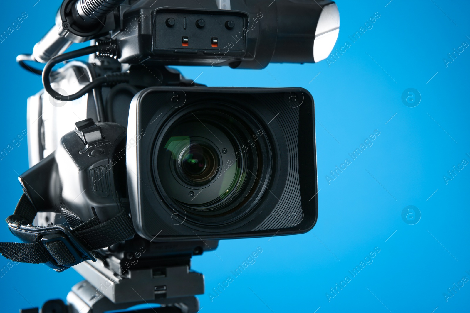 Photo of Professional video camera on blue background, closeup