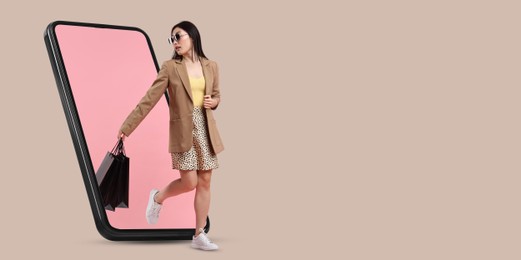 Image of Online shopping. Woman with paper bags walking out from smartphone on beige background, space for text. Banner design