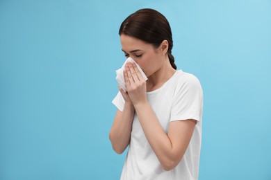 Photo of Woman blowing nose on light blue background. Cold symptoms