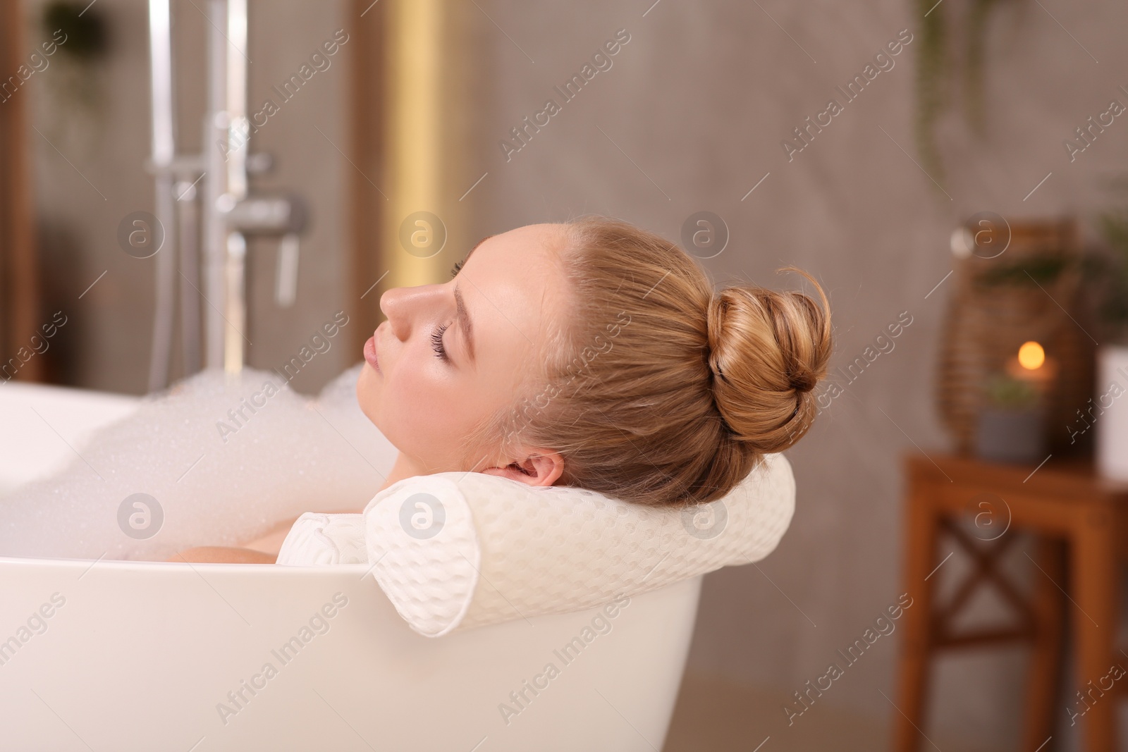 Photo of Young woman using pillow while enjoying bubble bath indoors