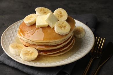 Photo of Delicious pancakes with bananas, butter and honey on dark table, closeup