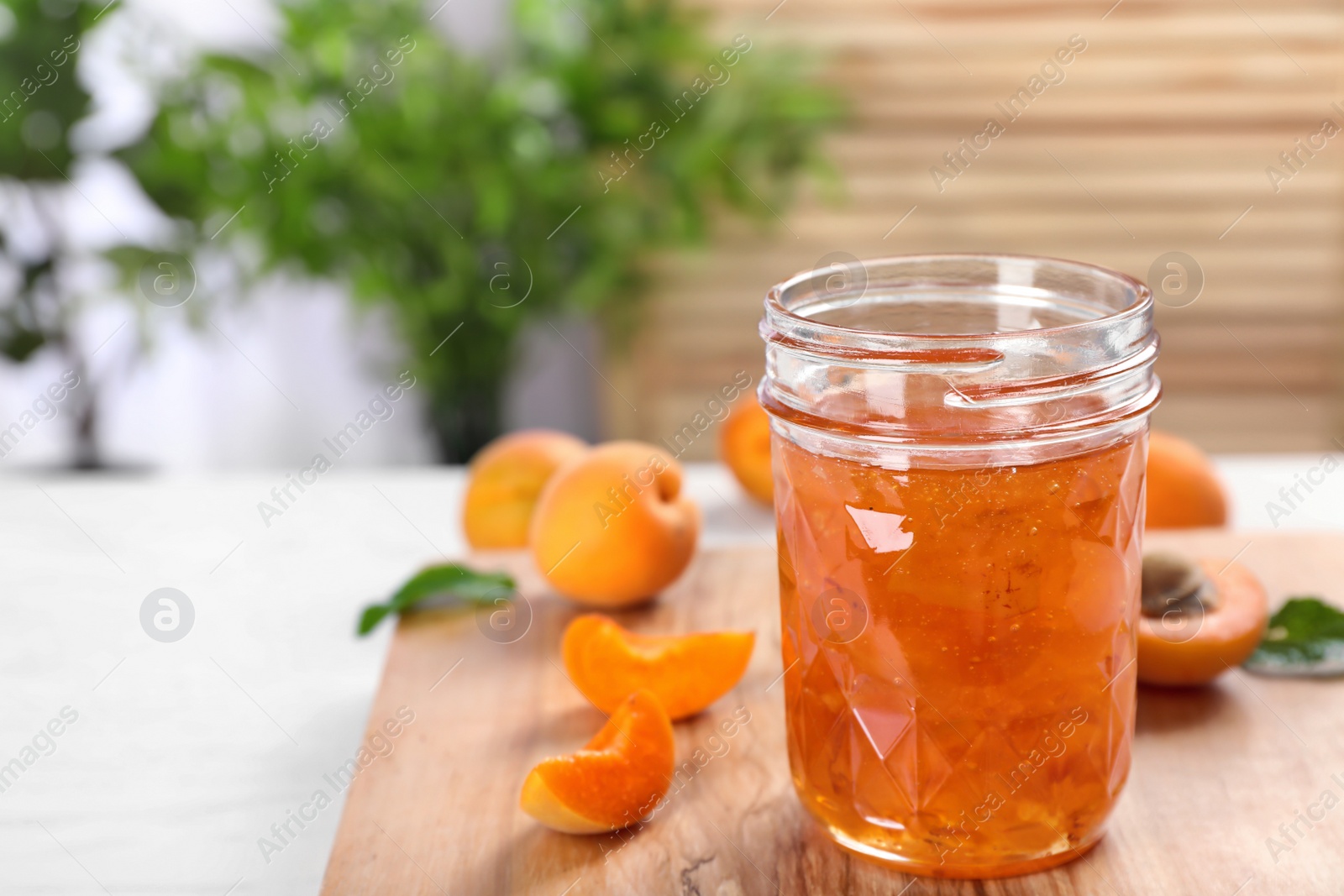 Photo of Jar with tasty apricot jam on wooden board