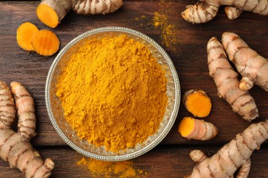 Plate with aromatic turmeric powder and cut roots on wooden table, flat lay