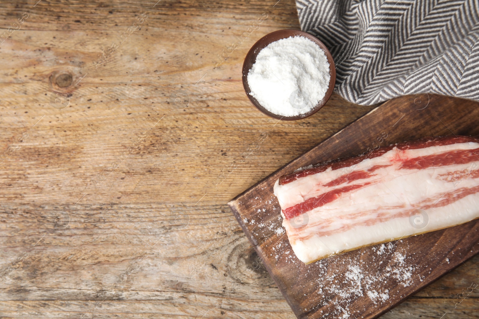 Photo of Board with bacon and salt on wooden background, flat lay. Space for text