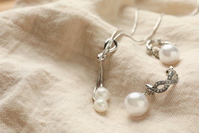 Photo of Elegant necklace and silver earrings with pearls on beige fabric, closeup