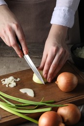 Woman cutting ripe onion at wooden table, closeup