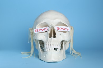 Photo of Information and media warfare concept. Human skull with noodles and words News in eye sockets on light blue background