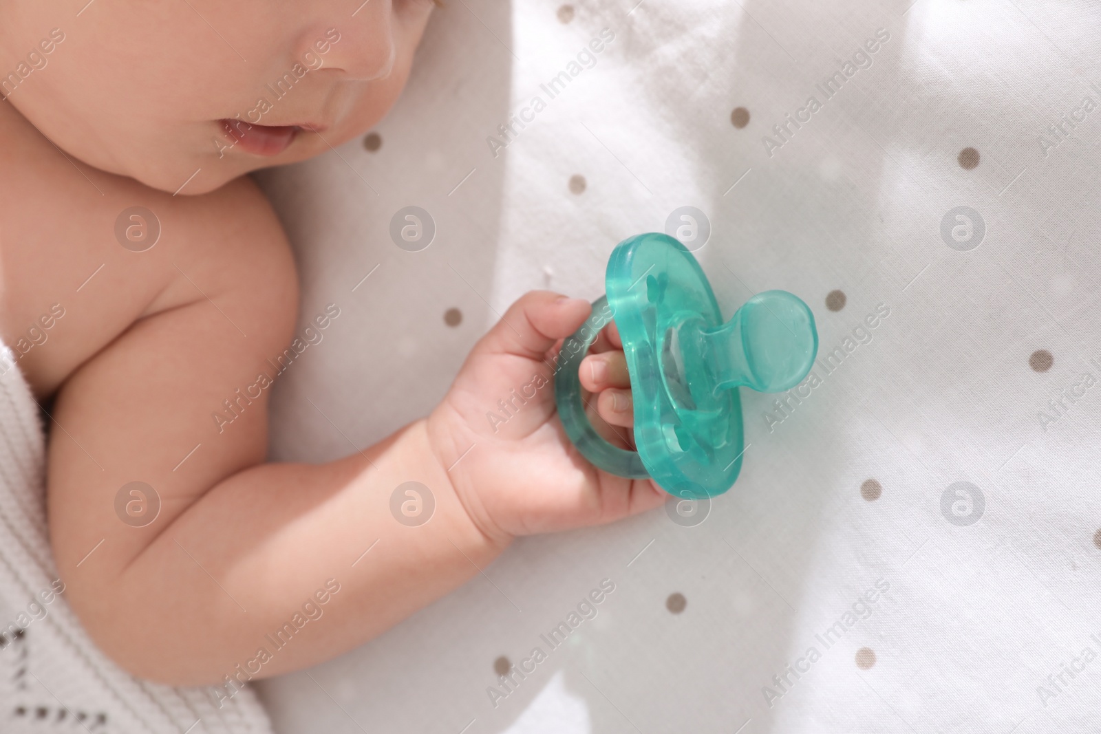 Photo of Little baby with pacifier in bed, closeup