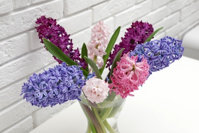 Photo of Beautiful hyacinths in glass vase on table against brick wall. Spring flowers