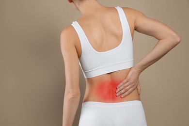 Woman suffering from pain in back on beige background, closeup