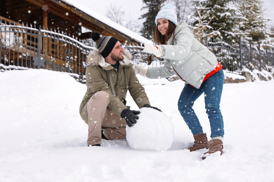 Photo of Happy couple making ball for snowman outdoors. Winter vacation