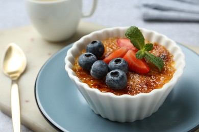 Delicious creme brulee with berries and mint in bowl served on grey table, closeup