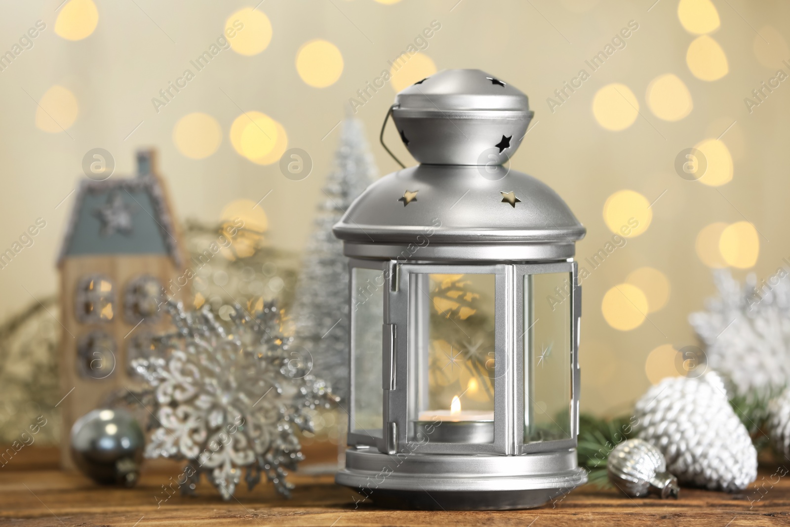 Photo of Christmas lantern with burning candle and festive decor on wooden table against blurred lights