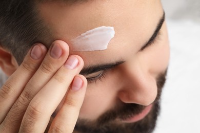 Man with dry skin applying cream onto his forehead on light background