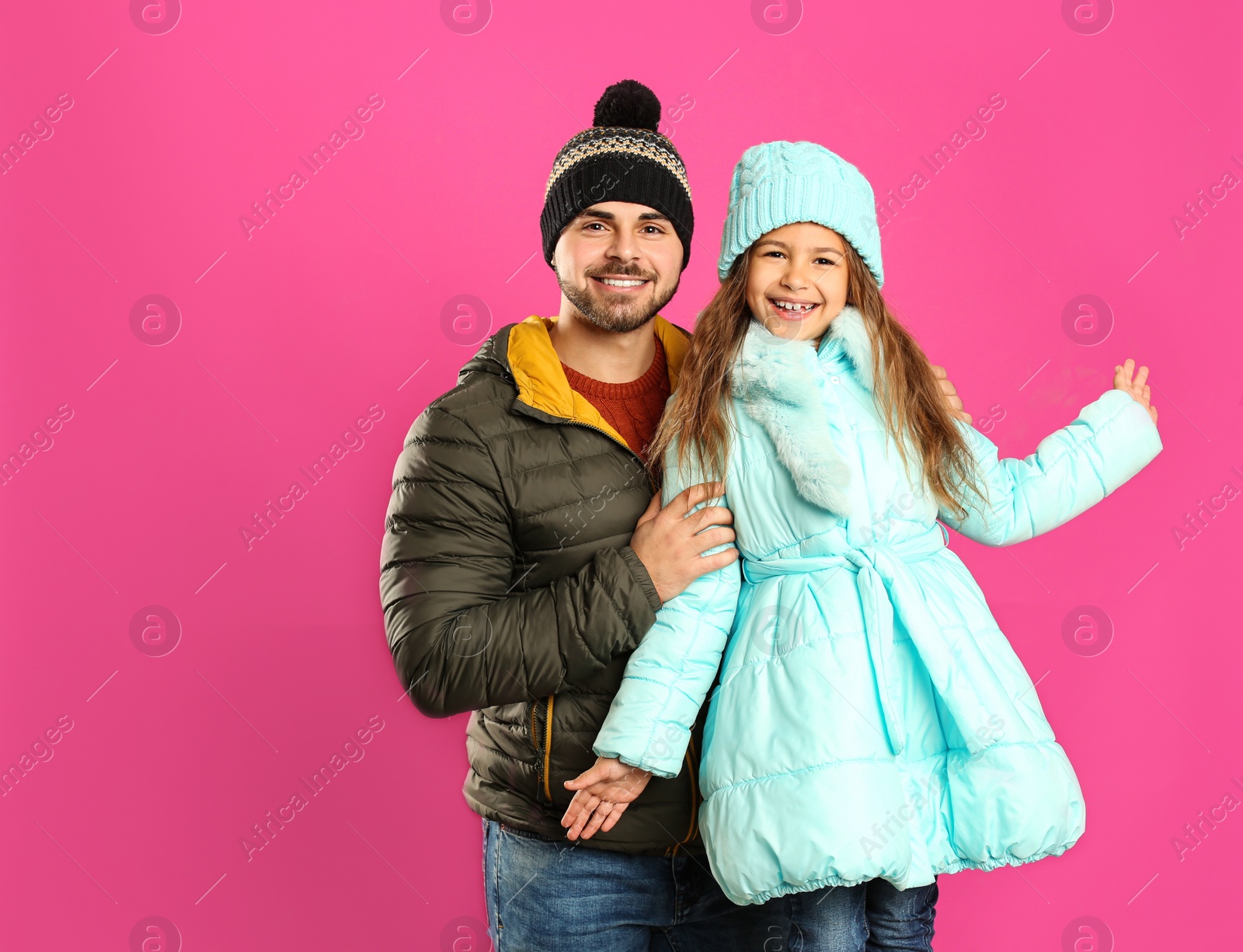 Photo of Happy father and daughter in warm clothes on pink background. Winter vacation