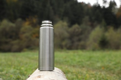 Photo of Metallic thermos on log outdoors, space for text