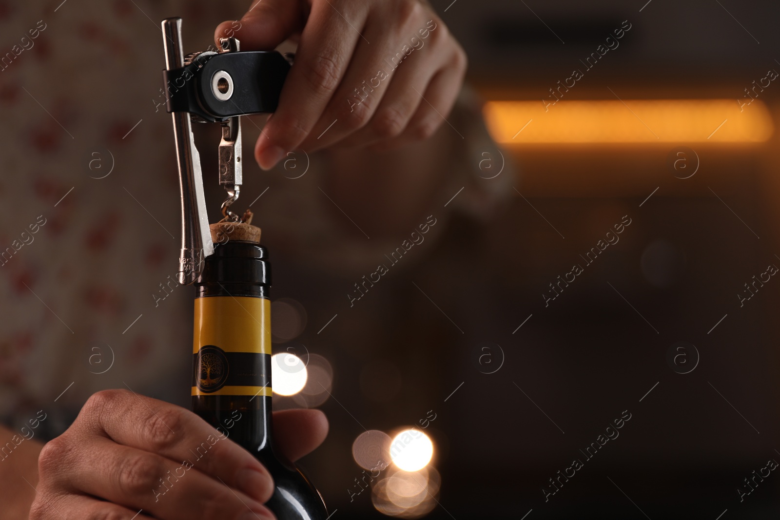 Photo of Woman opening wine bottle with corkscrew on blurred background, closeup. Space for text