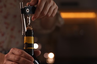 Woman opening wine bottle with corkscrew on blurred background, closeup. Space for text