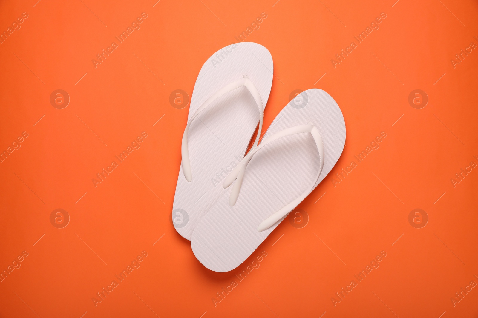 Photo of Stylish white flip flops on orange background, top view