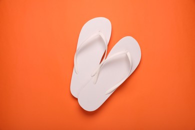 Photo of Stylish white flip flops on orange background, top view