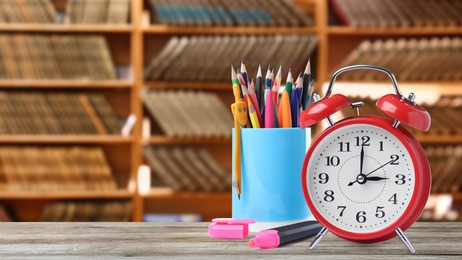 Image of Red alarm clock and different stationery on wooden table in library