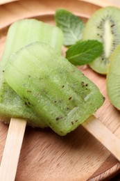 Tasty kiwi ice pops on wooden plate, closeup. Fruit popsicle