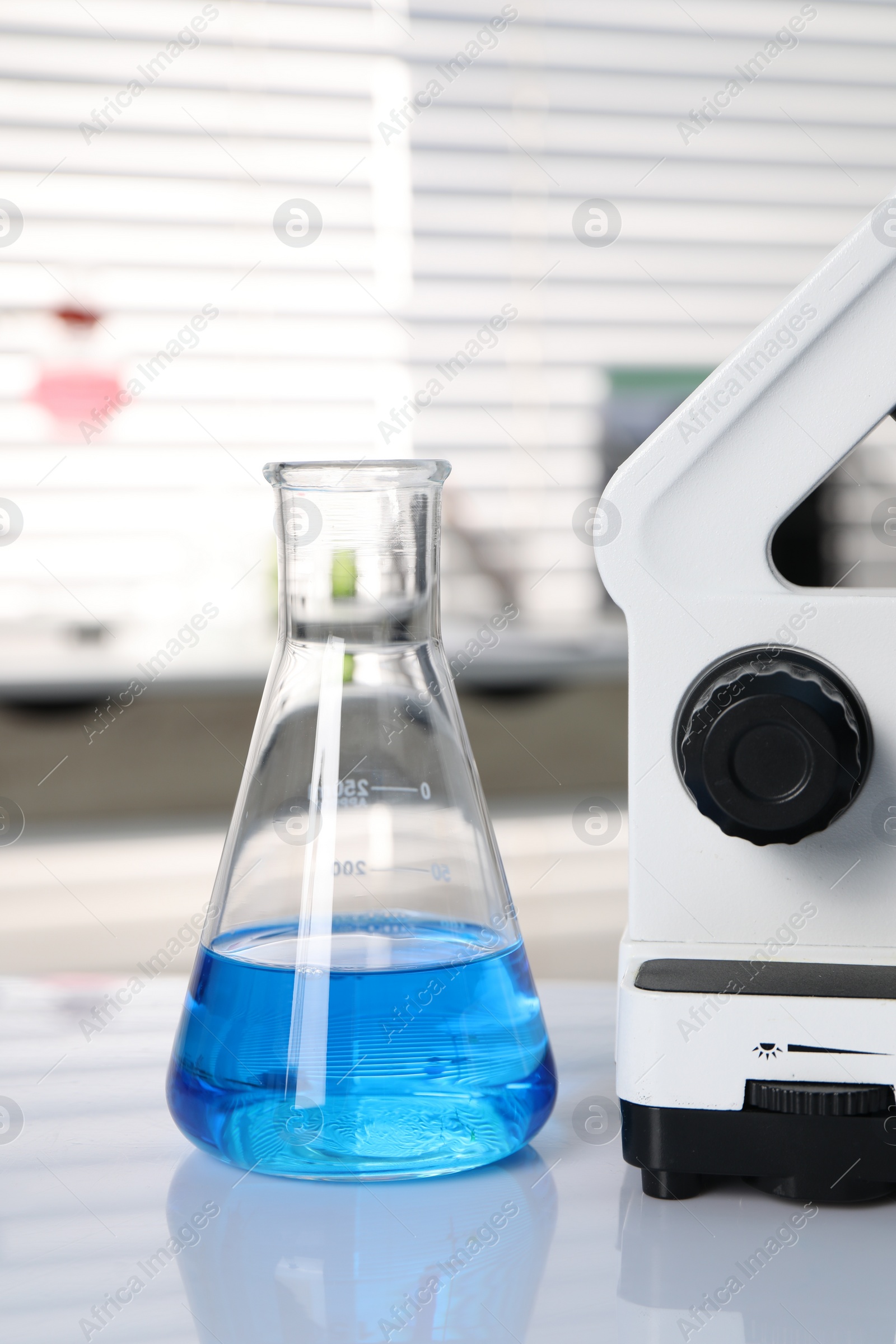 Photo of Laboratory analysis. Flask with blue liquid and microscope on white table indoors