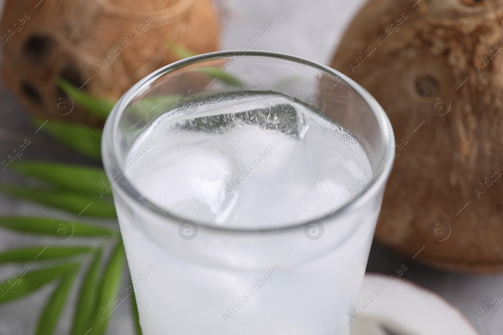 Photo of Glass of coconut water with ice cubes on grey table, closeup