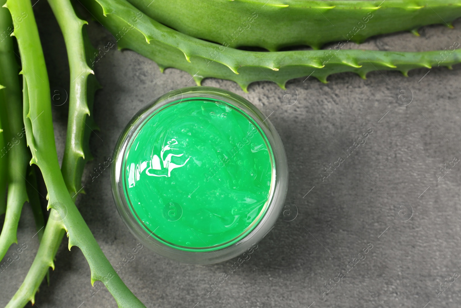 Photo of Bowl with natural gel and aloe vera leaves on grey table, flat lay