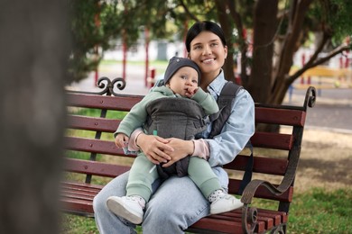 Photo of Mother holding her child in sling (baby carrier) on bench in park