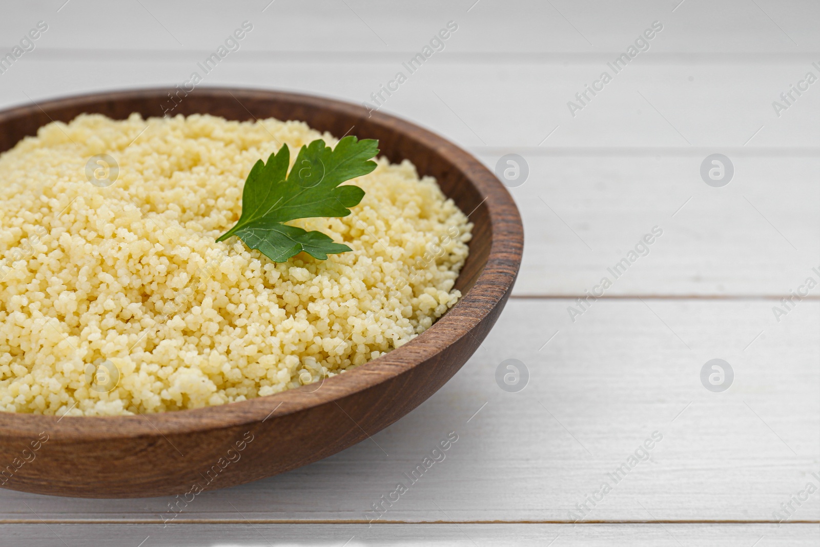 Photo of Tasty couscous with parsley on white wooden table, closeup. Space for text
