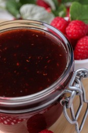 Glass jar of delicious raspberry jam on table, closeup