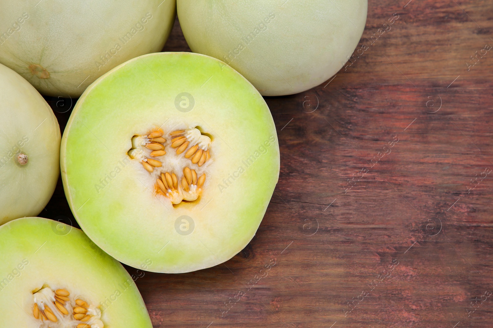 Photo of Whole and cut fresh ripe melons on wooden table, flat lay. Space for text