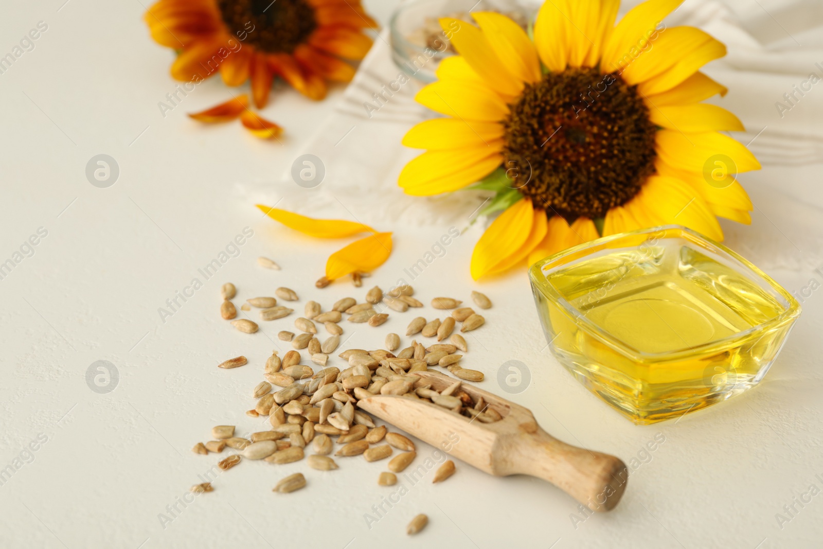 Photo of Sunflower oil in glass bowl and seeds on white table