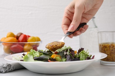 Photo of Woman pouring tasty vinegar based sauce (Vinaigrette) into plate with salad at light table, closeup