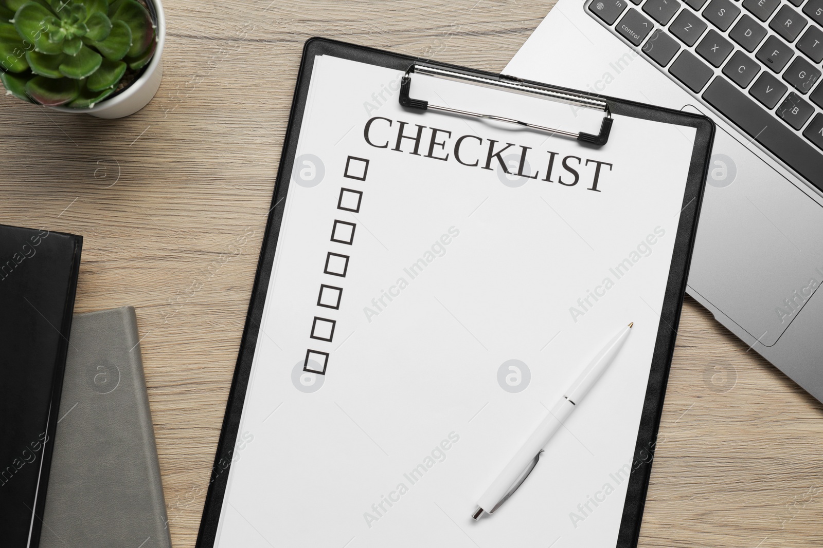 Photo of Clipboard with checklist, pen and laptop on wooden table, flat lay