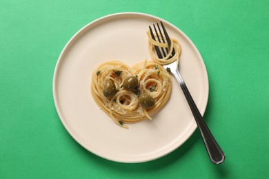Photo of Heart made of tasty spaghetti, fork, olives and cheese on green background, top view