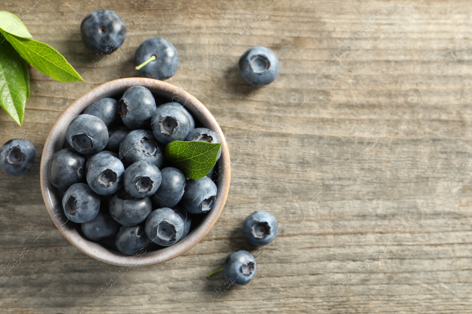 Photo of Bowl of tasty fresh blueberries with leaves on wooden table, flat lay. Space for text