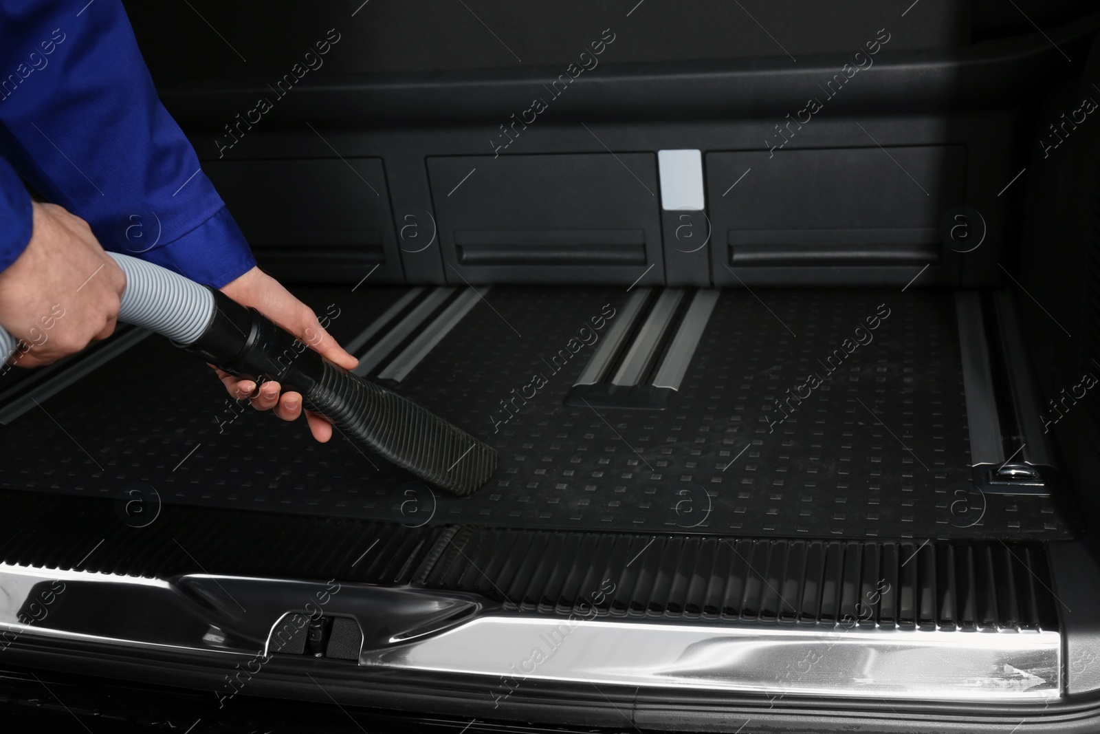 Photo of Worker using vacuum cleaner in automobile trunk at car wash, closeup