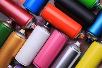 Photo of Cans of different graffiti spray paints on color background, flat lay