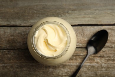 Photo of Jar of delicious mayonnaise and spoon on wooden table, flat lay