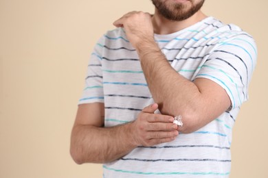 Photo of Man applying cream onto elbow on beige background, closeup. Space for text