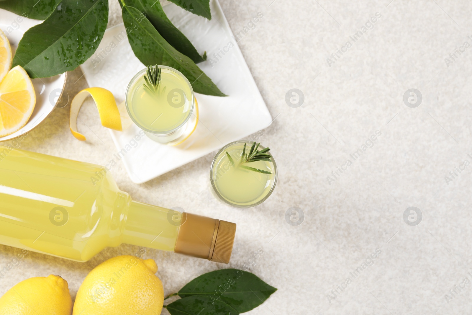 Photo of Tasty limoncello liqueur, lemons and green leaves on light textured table, flat lay. Space for text